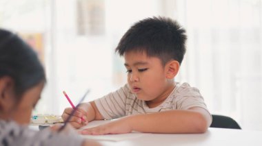 Bir çocuk bir kağıt parçasına pembe bir kalemle yazıyor. O işine odaklanmış ve eğleniyor gibi görünüyor. Sahne penceresi olan bir odada geçiyor.