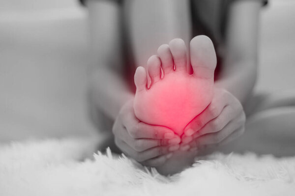 У женщины босиком болит, когда она сидит дома на диване. Боль в ногах из-за фасциита Плантара и длительного пробуждения. Здоровье и медицинская концепция