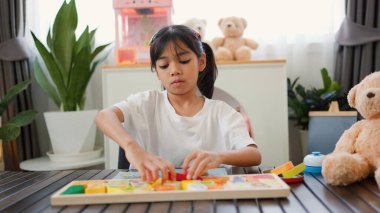 Evde renkli bulmaca bloklarıyla oynayan Asyalı kız, yaratıcı ve dokunsal öğrenme faaliyetleri yoluyla erken çocukluk eğitimi, beyin gelişimi ve bilişsel becerileri teşvik ediyor..