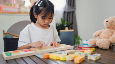 Evde renkli bulmaca bloklarıyla oynayan Asyalı kız, yaratıcı ve dokunsal öğrenme faaliyetleri yoluyla erken çocukluk eğitimi, beyin gelişimi ve bilişsel becerileri teşvik ediyor..