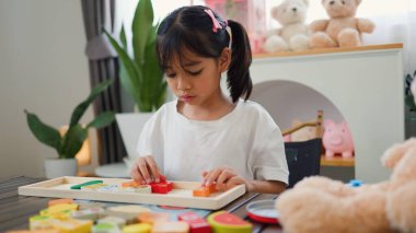 Evde renkli bulmaca bloklarıyla oynayan Asyalı kız, yaratıcı ve dokunsal öğrenme faaliyetleri yoluyla erken çocukluk eğitimi, beyin gelişimi ve bilişsel becerileri teşvik ediyor..
