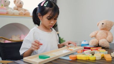 Evde renkli bulmaca bloklarıyla oynayan Asyalı kız, yaratıcı ve dokunsal öğrenme faaliyetleri yoluyla erken çocukluk eğitimi, beyin gelişimi ve bilişsel becerileri teşvik ediyor..