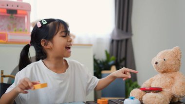 Asyalı kız evde oyuncak ayı ve oyuncak yemekle oynuyormuş gibi yapıyor. Yaratıcılığı, sosyal becerileri ve erken çocukluk gelişimini yaratıcı öğrenme faaliyetleri yoluyla teşvik etmek.
