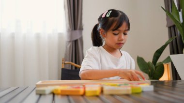 Evde renkli bulmaca bloklarıyla oynayan Asyalı kız, yaratıcı ve dokunsal öğrenme faaliyetleri yoluyla erken çocukluk eğitimi, beyin gelişimi ve bilişsel becerileri teşvik ediyor..