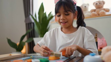 Evde renkli bulmaca bloklarıyla oynayan Asyalı kız, yaratıcı ve dokunsal öğrenme faaliyetleri yoluyla erken çocukluk eğitimi, beyin gelişimi ve bilişsel becerileri teşvik ediyor..