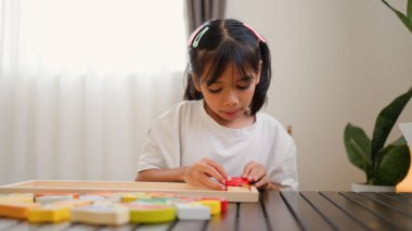 Evde renkli bulmaca bloklarıyla oynayan Asyalı kız, yaratıcı ve dokunsal öğrenme faaliyetleri yoluyla erken çocukluk eğitimi, beyin gelişimi ve bilişsel becerileri teşvik ediyor..