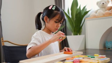 Evde renkli bulmaca bloklarıyla oynayan Asyalı kız, yaratıcı ve dokunsal öğrenme faaliyetleri yoluyla erken çocukluk eğitimi, beyin gelişimi ve bilişsel becerileri teşvik ediyor..