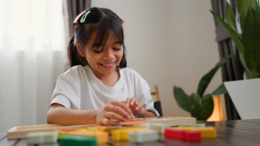 Evde renkli bulmaca bloklarıyla oynayan Asyalı kız, yaratıcı ve dokunsal öğrenme faaliyetleri yoluyla erken çocukluk eğitimi, beyin gelişimi ve bilişsel becerileri teşvik ediyor..