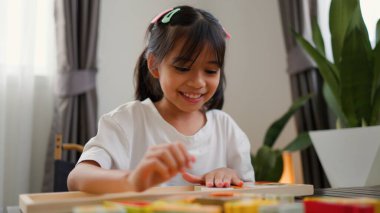 Evde renkli bulmaca bloklarıyla oynayan Asyalı kız, yaratıcı ve dokunsal öğrenme faaliyetleri yoluyla erken çocukluk eğitimi, beyin gelişimi ve bilişsel becerileri teşvik ediyor..