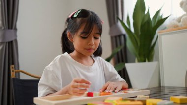 Evde renkli bulmaca bloklarıyla oynayan Asyalı kız, yaratıcı ve dokunsal öğrenme faaliyetleri yoluyla erken çocukluk eğitimi, beyin gelişimi ve bilişsel becerileri teşvik ediyor..