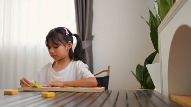 Evde renkli bulmaca bloklarıyla oynayan Asyalı kız, yaratıcı ve dokunsal öğrenme faaliyetleri yoluyla erken çocukluk eğitimi, beyin gelişimi ve bilişsel becerileri teşvik ediyor..