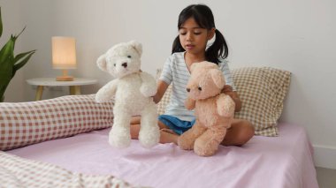 Sıcak yatak odasında oyuncak ayılarla oynayan tatlı Asyalı kız sıcak ve doğal bir ev atmosferinde hayal gücünü ve çocukluk masumiyetini ifade ediyor..