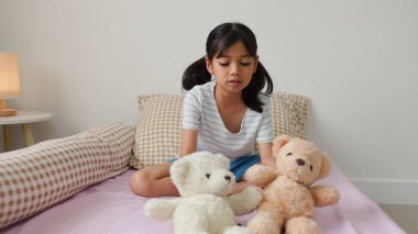 Sıcak yatak odasında oyuncak ayılarla oynayan tatlı Asyalı kız sıcak ve doğal bir ev atmosferinde hayal gücünü ve çocukluk masumiyetini ifade ediyor..