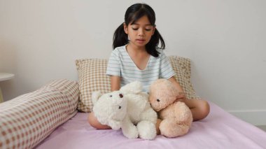 Sıcak yatak odasında oyuncak ayılarla oynayan tatlı Asyalı kız sıcak ve doğal bir ev atmosferinde hayal gücünü ve çocukluk masumiyetini ifade ediyor..