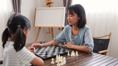 Evde satranç oynayan iki Asyalı kız çocuk gelişimi, eğitim ve kardeş kaynaşması kavramları için mükemmel, eğlenceli ve stratejik düşüncelerini ifade ediyorlar..