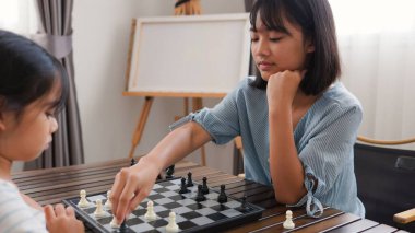 Evde satranç oynayan iki Asyalı kız çocuk gelişimi, eğitim ve kardeş kaynaşması kavramları için mükemmel, eğlenceli ve stratejik düşüncelerini ifade ediyorlar..