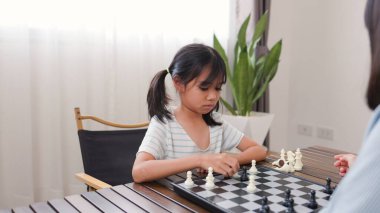 Evde satranç oynayan iki Asyalı kız kardeş, beyin becerilerini geliştirmek, mantıklı düşünmek, ve eğlenceli stratejik oyunlarla iç mekanda öğrenme ortamında bağ kurmak..