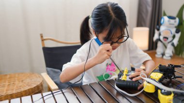 Asyalı kız evde robot parçaları birleştiriyor, BTMM ve elektronik aletleri öğreniyor. Mühendislik becerileri, mantıksal düşünme ve çocuklara uygulamalı kodlama eğitimi yoluyla problem çözme.