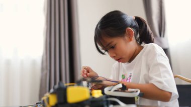 Asyalı kız evde robot parçaları birleştiriyor, BTMM ve elektronik aletleri öğreniyor. Mühendislik becerileri, mantıksal düşünme ve çocuklara uygulamalı kodlama eğitimi yoluyla problem çözme.