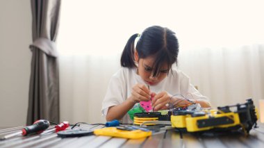 Asyalı kız evde robot parçaları birleştiriyor, BTMM ve elektronik aletleri öğreniyor. Mühendislik becerileri, mantıksal düşünme ve çocuklara uygulamalı kodlama eğitimi yoluyla problem çözme.