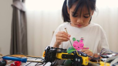 Asyalı kız evde robot parçaları birleştiriyor, BTMM ve elektronik aletleri öğreniyor. Mühendislik becerileri, mantıksal düşünme ve çocuklara uygulamalı kodlama eğitimi yoluyla problem çözme.