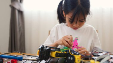 Asyalı kız evde robot parçaları birleştiriyor, BTMM ve elektronik aletleri öğreniyor. Mühendislik becerileri, mantıksal düşünme ve çocuklara uygulamalı kodlama eğitimi yoluyla problem çözme.
