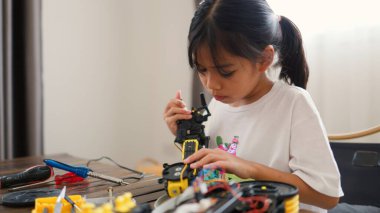 Asyalı kız evde robot parçaları birleştiriyor, BTMM ve elektronik aletleri öğreniyor. Mühendislik becerileri, mantıksal düşünme ve çocuklara uygulamalı kodlama eğitimi yoluyla problem çözme.