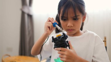 Asyalı kız evde robot parçaları birleştiriyor, BTMM ve elektronik aletleri öğreniyor. Mühendislik becerileri, mantıksal düşünme ve çocuklara uygulamalı kodlama eğitimi yoluyla problem çözme.