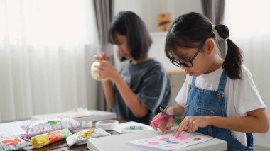 Evde yaratıcı DIY aktivitesi yapan Asyalı kızlar sanat malzemeleri, makas ve konsantrasyonla evde eğitim ortamında beceri ve hayal gücü geliştiriyorlar..