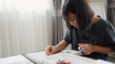 İki Asyalı kız, sıcak ve odaklı bir atmosferle evde eğitim, yaratıcılık ve modern eğitimi temsil ederek, parlak bir odada okuyor ve resim çiziyor..