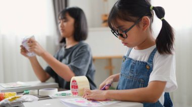 Evde yaratıcı DIY aktivitesi yapan Asyalı kızlar sanat malzemeleri, makas ve konsantrasyonla evde eğitim ortamında beceri ve hayal gücü geliştiriyorlar..