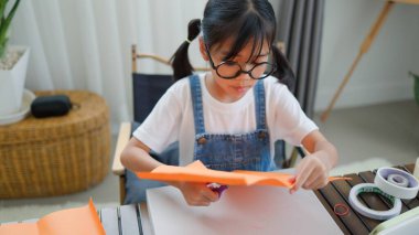 Asyalı kız evde pusula ve renkli bir kağıt kullanarak yaratıcılığı, motor becerileri ve ev okulunda eğlenceli öğrenmeyi destekleyen bir DIY zanaat projesi yapmaya odaklanmış..