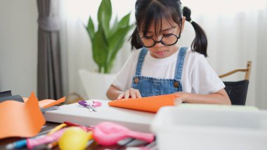 Asyalı kız evde pusula ve renkli bir kağıt kullanarak yaratıcılığı, motor becerileri ve ev okulunda eğlenceli öğrenmeyi destekleyen bir DIY zanaat projesi yapmaya odaklanmış..
