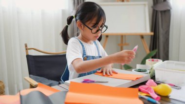 Asyalı kız evde pusula ve renkli bir kağıt kullanarak yaratıcılığı, motor becerileri ve ev okulunda eğlenceli öğrenmeyi destekleyen bir DIY zanaat projesi yapmaya odaklanmış..