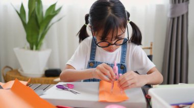 Asyalı kız evde pusula ve renkli bir kağıt kullanarak yaratıcılığı, motor becerileri ve ev okulunda eğlenceli öğrenmeyi destekleyen bir DIY zanaat projesi yapmaya odaklanmış..