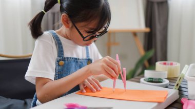 Asyalı kız evde pusula ve renkli bir kağıt kullanarak yaratıcılığı, motor becerileri ve ev okulunda eğlenceli öğrenmeyi destekleyen bir DIY zanaat projesi yapmaya odaklanmış..