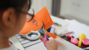 Asyalı kız evde pusula ve renkli bir kağıt kullanarak yaratıcılığı, motor becerileri ve ev okulunda eğlenceli öğrenmeyi destekleyen bir DIY zanaat projesi yapmaya odaklanmış..