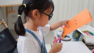 Asyalı kız evde pusula ve renkli bir kağıt kullanarak yaratıcılığı, motor becerileri ve ev okulunda eğlenceli öğrenmeyi destekleyen bir DIY zanaat projesi yapmaya odaklanmış..