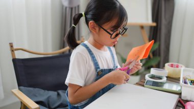 Asyalı kız evde pusula ve renkli bir kağıt kullanarak yaratıcılığı, motor becerileri ve ev okulunda eğlenceli öğrenmeyi destekleyen bir DIY zanaat projesi yapmaya odaklanmış..
