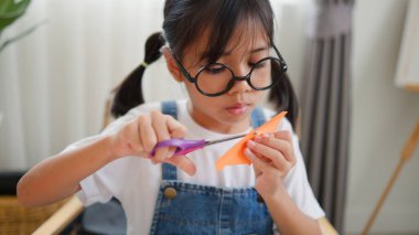 Asyalı kız evde pusula ve renkli bir kağıt kullanarak yaratıcılığı, motor becerileri ve ev okulunda eğlenceli öğrenmeyi destekleyen bir DIY zanaat projesi yapmaya odaklanmış..