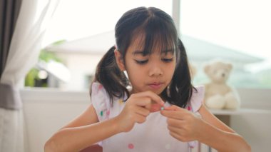 Asyalı kız evde renkli boncuklara iplik geçirip sakin bir ortamda konsantrasyonu, yaratıcılığı ve iyi motor becerileri arttıran eğlenceli ve eğitici bir aktiviteye odaklanıyor..