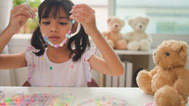 Asyalı kız evde renkli boncuklara iplik geçirip sakin bir ortamda konsantrasyonu, yaratıcılığı ve iyi motor becerileri arttıran eğlenceli ve eğitici bir aktiviteye odaklanıyor..