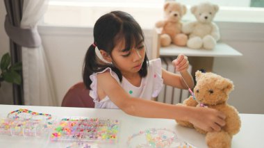 Asyalı kız evde renkli boncuklara iplik geçirip sakin bir ortamda konsantrasyonu, yaratıcılığı ve iyi motor becerileri arttıran eğlenceli ve eğitici bir aktiviteye odaklanıyor..