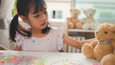 Asyalı kız evde renkli boncuklara iplik geçirip sakin bir ortamda konsantrasyonu, yaratıcılığı ve iyi motor becerileri arttıran eğlenceli ve eğitici bir aktiviteye odaklanıyor..