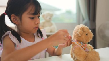 Asyalı kız evde renkli boncuklara iplik geçirip sakin bir ortamda konsantrasyonu, yaratıcılığı ve iyi motor becerileri arttıran eğlenceli ve eğitici bir aktiviteye odaklanıyor..