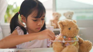Asyalı kız evde renkli boncuklara iplik geçirip sakin bir ortamda konsantrasyonu, yaratıcılığı ve iyi motor becerileri arttıran eğlenceli ve eğitici bir aktiviteye odaklanıyor..