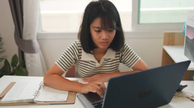 Evde online öğrenim için dizüstü bilgisayar kullanan Asyalı kız, sakin ve odaklı bir çalışma ortamında uzaktan eğitimi, ev okulunu ve dijital beceri geliştirmeyi temsil ediyor.