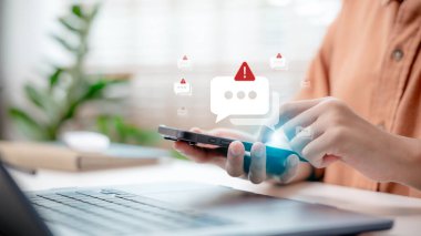 Kapalı çekimde elinde spam uyarı simgesi olan akıllı telefon, online dolandırıcılık uyarısı konsepti, sahte mesaj, siber güvenlik ve mobil güvenlik tebligatı.
