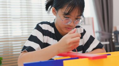 Asyalı kız, mekanik parçaları odaklanma ve kararlılıkla birleştirerek BTMM öğreniyor. Evde uygulamalı eğitim, çocuk mühendisliği, yaratıcılık ve bilim eğitimi kavramı.