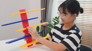 Asyalı kız, mekanik parçaları odaklanma ve kararlılıkla birleştirerek BTMM öğreniyor. Evde uygulamalı eğitim, çocuk mühendisliği, yaratıcılık ve bilim eğitimi kavramı.